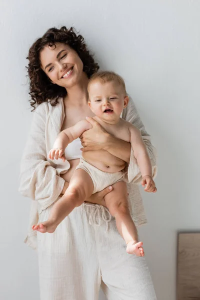 Mujer feliz en pijama sosteniendo a la niña en casa - foto de stock