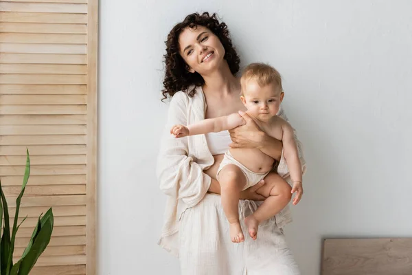 Lächelnde brünette Mutter hält ihre kleine Tochter zu Hause — Stockfoto