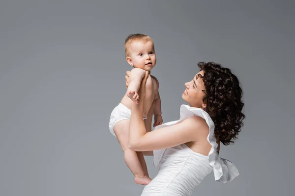 Mother in stylish dress holding infant daughter in panties isolated on grey — Stock Photo