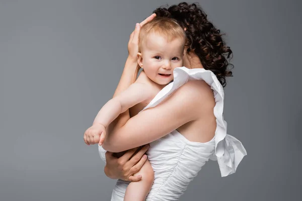 Frau im Kleid umarmt lächelnde kleine Tochter isoliert auf grau — Stockfoto