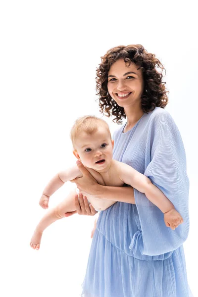 Mujer sonriente en vestido azul sosteniendo niña aislada en blanco - foto de stock