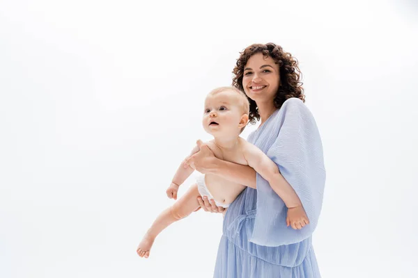 Donna allegra in abito blu guardando la fotocamera mentre tiene la bambina isolata sul bianco — Foto stock