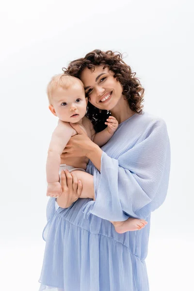 Happy parent in blue dress looking at camera and touching baby daughter isolated on white — Stock Photo