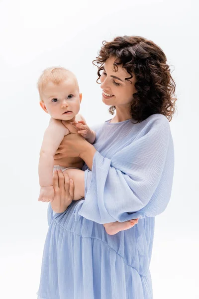 Mujer positiva en vestido azul mirando a la hija bebé aislado en blanco — Stock Photo