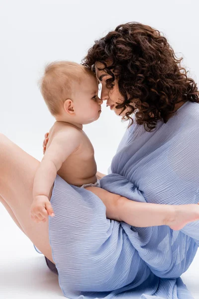 Vista lateral de mamá en vestido sosteniendo la nariz de la niña a la nariz sobre fondo blanco - foto de stock