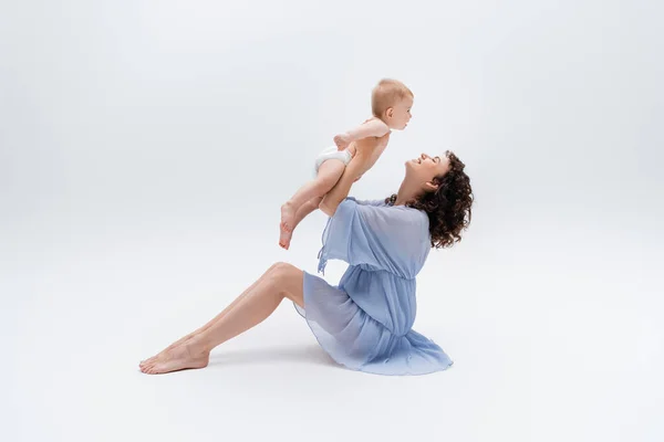 Vista lateral de mujer descalza en vestido jugando con niña sobre fondo blanco - foto de stock