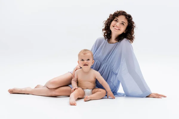 Lächelnde Eltern im Kleid berühren Baby-Tochter, während sie auf weißem Hintergrund sitzen — Stockfoto
