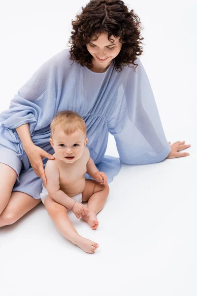 Vue grand angle du parent bouclé touchant bébé fille souriante tout en étant assis sur fond blanc — Photo de stock