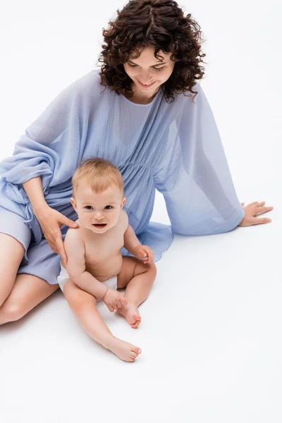 High angle view of curly parent touching smiling baby girl while sitting on white background — Stock Photo