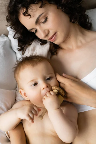 Вид сверху на девочку, держащую игрушку рядом с мамой на кровати утром — стоковое фото