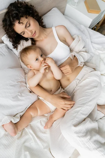 Vue du dessus de la femme brune étreignant bébé avec un jouet en bois sur le lit — Photo de stock