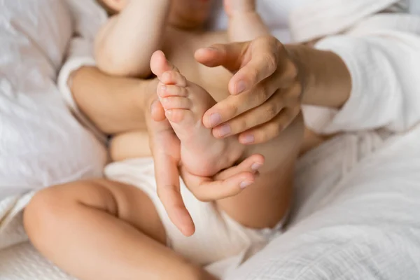 Vista recortada de la madre tocando el pie de la hija bebé en la cama - foto de stock