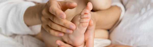 Vista cortada da mulher tocando o pé da filha infantil na cama embaçada, banner — Fotografia de Stock