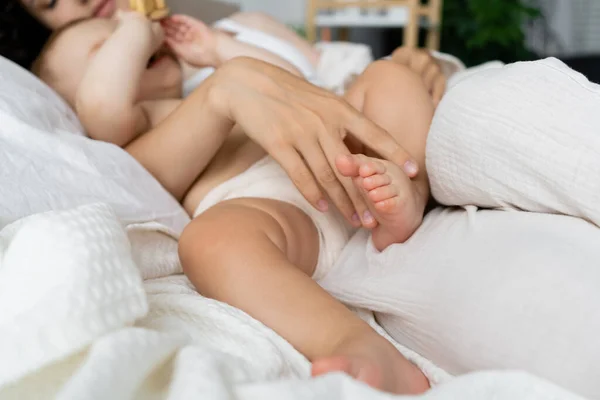 Blurred woman touching leg of baby girl on bed in morning — Stock Photo