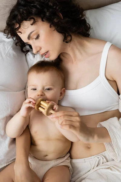 Top view of mother in pajamas holding toy near infant daughter on bed — Stock Photo