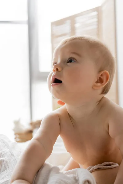 Bébé fille regardant loin tout en étant assis près de maman sur lit flou — Photo de stock