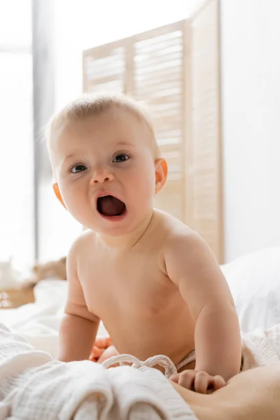 Säugling gähnt und blickt in die Kamera nahe der Mutter auf dem Bett — Stockfoto