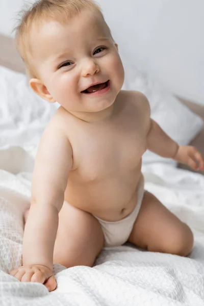 Infant girl in panties smiling at camera while sitting on bed — Stock Photo