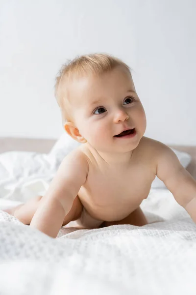 Portrait of pleased baby girl looking away on white bedding at home — Stock Photo