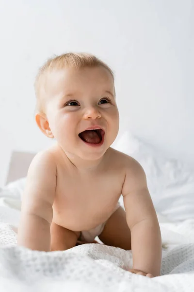 Emocionada niña mirando hacia otro lado en ropa de cama blanca en casa - foto de stock