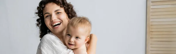 Cheerful woman hugging baby daughter at home, banner — Stock Photo
