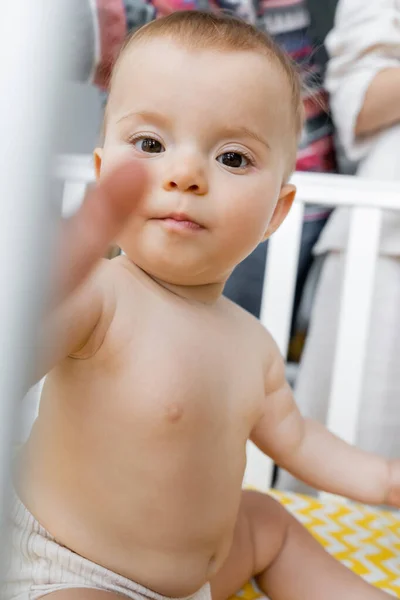 Baby schaut in Kamera, während es im Kinderbett im Schlafzimmer sitzt — Stockfoto