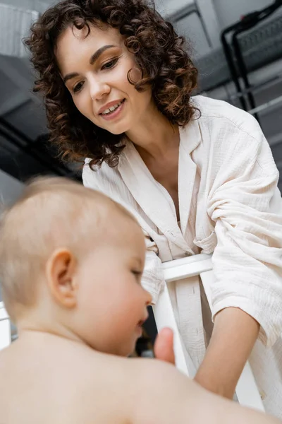 Low angle view of smiling woman taking blurred baby daughter from crib at home — Stock Photo