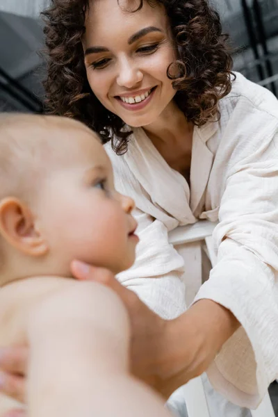 Niedriger Blickwinkel der glücklichen brünetten Mutter, die verschwommenes Babymädchen von der Krippe nimmt — Stockfoto