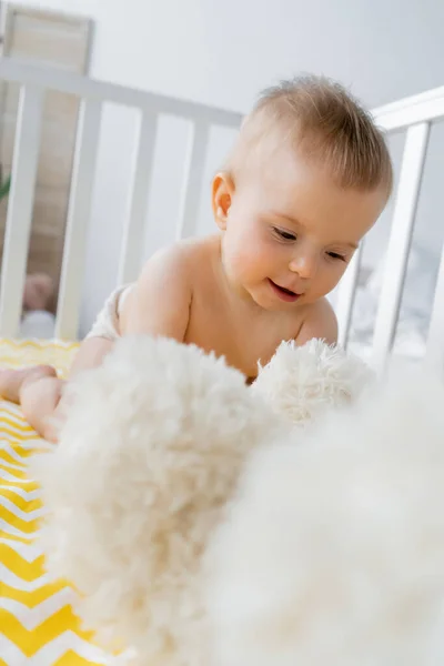 Infant girl looking at blurred soft toy in baby crib at home — Stock Photo