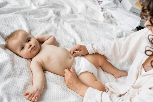 Visão de alto ângulo da mãe usando fralda na filha do bebê na cama — Fotografia de Stock
