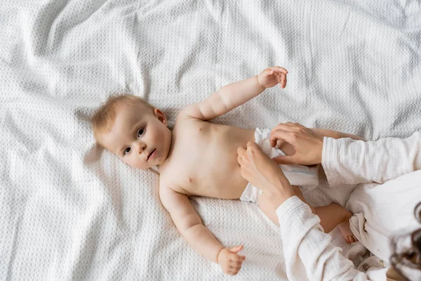 Вид сверху на родителя, меняющего подгузник на новорожденной дочери на кровати дома — стоковое фото