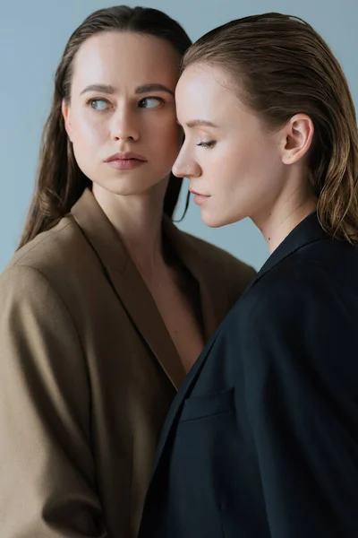 Lesbian woman in beige blazer looking away near young girlfriend isolated on grey — Stock Photo