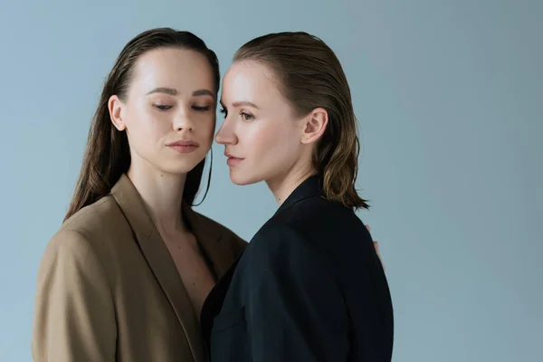 Young lesbian couple in beige and black blazers standing isolated on grey — Stock Photo