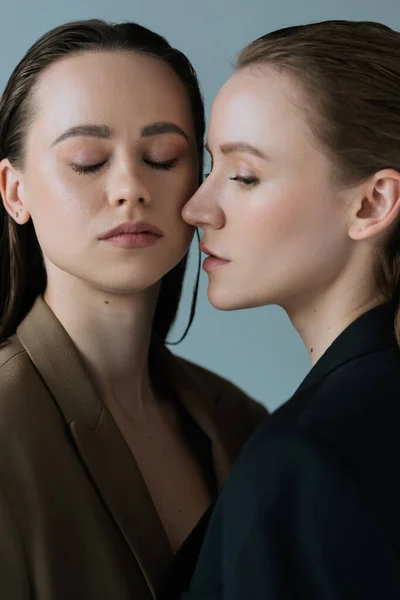 Jeune femme aux yeux fermés et sa copine lesbienne isolée sur gris — Photo de stock