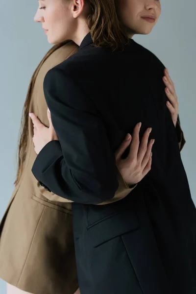 Cropped view of young lesbian women in beige and black blazers embracing isolated on grey — Stock Photo