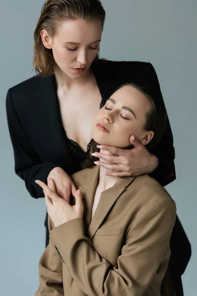 Sexy lesbiana mujer en negro sujetador y chaqueta seducir joven novia aislado en gris - foto de stock