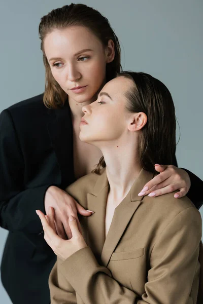 Hübsche lesbische Frau umarmt junge brünette Freundin isoliert auf grau — Stockfoto