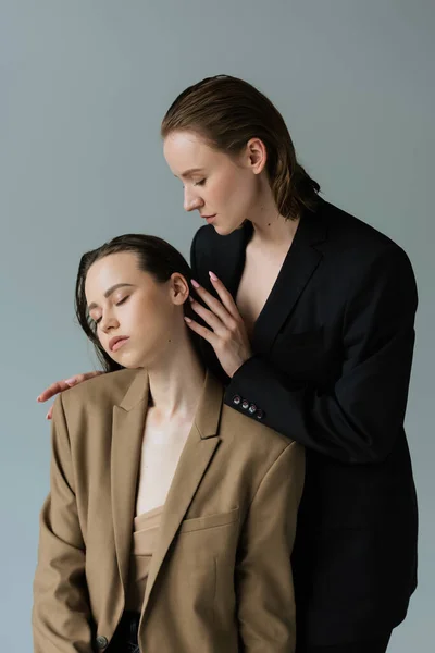 Pretty lesbian woman touching hair of young brunette girlfriend isolated on grey — Stock Photo