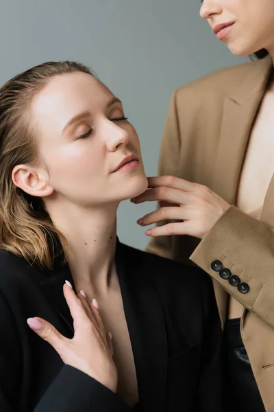 Lesbienne femme avec les yeux fermés près de jeune copine toucher son menton isolé sur gris — Photo de stock