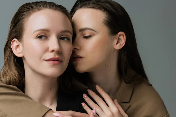 Brunette woman with closed eyes near young lesbian girlfriend looking away isolated on grey — Stock Photo