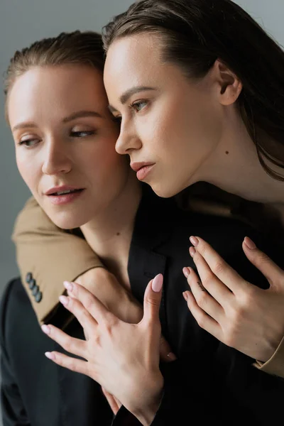 Jolie brune femme étreignant jeune lesbienne partenaire isolé sur gris — Photo de stock