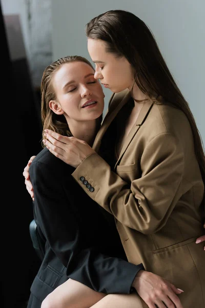 Jeune femme aux cheveux longs assis sur des tours de copine lesbienne avec les yeux fermés sur fond gris — Photo de stock