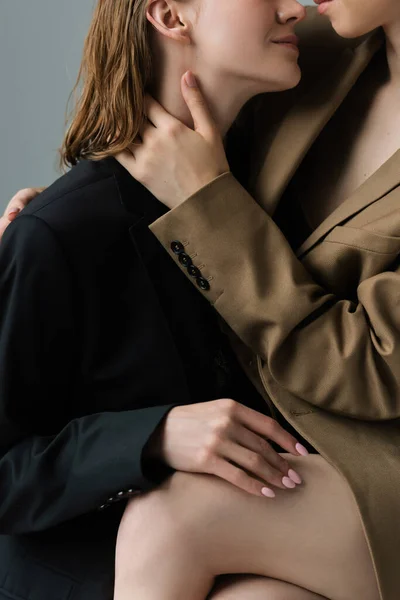 Partial view of same sex lesbian couple in beige and black blazers embracing isolated on grey — Stock Photo