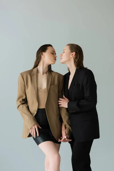 Same sex lesbian couple in blazers holding hands and looking at each other isolated on grey — Stock Photo