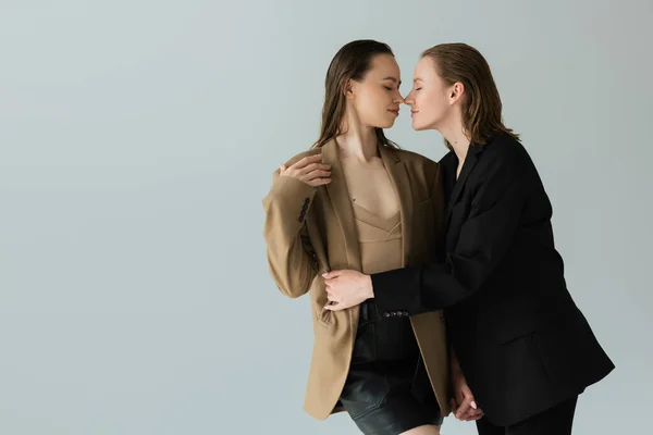 Young lesbian woman holding hands with smiling girlfriend and hugging her isolated on grey — Stock Photo