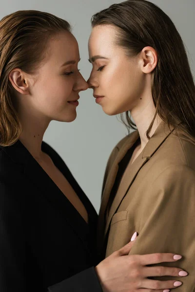 Side view of lesbian partners with closed eyes standing face to face isolated on grey — Stock Photo