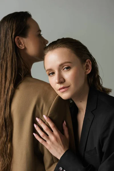 Bonita lesbiana mujer mirando cámara cerca lesbiana novia con largo pelo aislado en gris - foto de stock