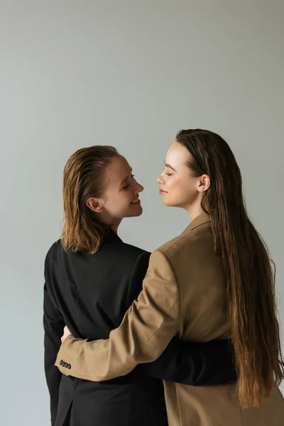 Back view of lesbian couple in jackets embracing and smiling at each other isolated on grey — Stock Photo