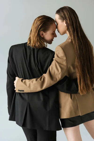 Back view of woman with long hair embracing young lesbian girlfriend isolated on grey — Stock Photo