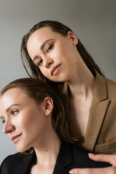 Brunette woman looking at camera near smiling lesbian girlfriend isolated on grey — Stock Photo